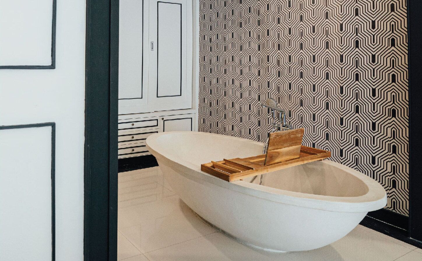 A modern bathroom with a freestanding bathtub, a wooden shelf, and a patterned wall.