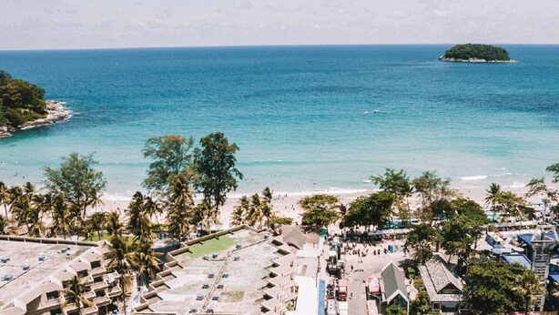 Un hotel frente al mar con vista a la playa, varios balcones y una pequeña isla en la distancia.