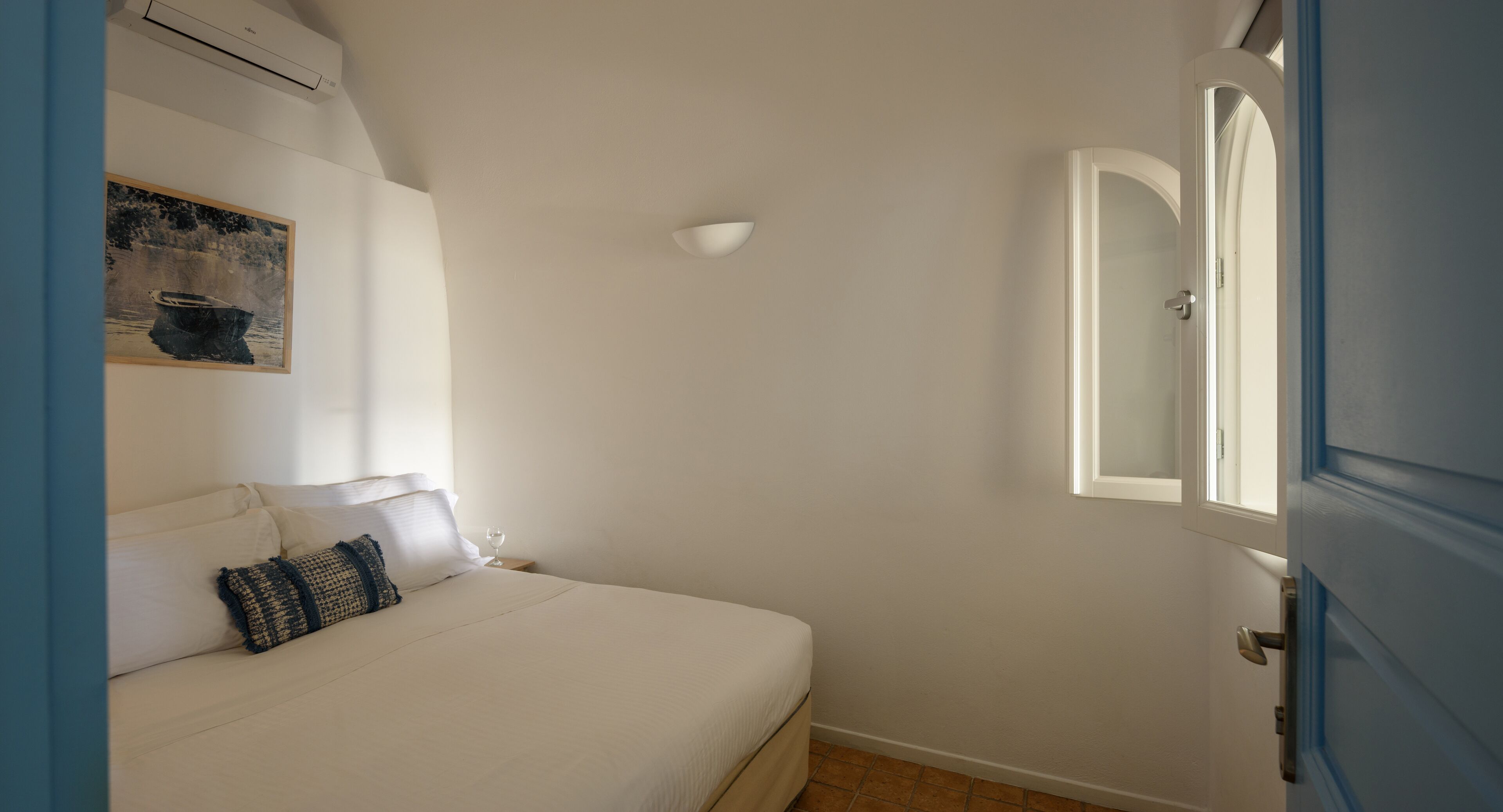 A bedroom with a bed, a nightstand, a wall-mounted air conditioner, a painting, and a door.