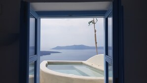 A room with a bathtub and a view of a body of water and distant land. - Pantelia Suites (Santorini)