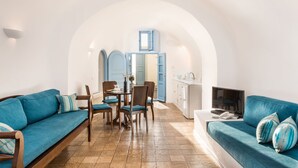 A modern living room with a sofa, dining table, chairs, and a TV. - Pantelia Suites (Santorini)
