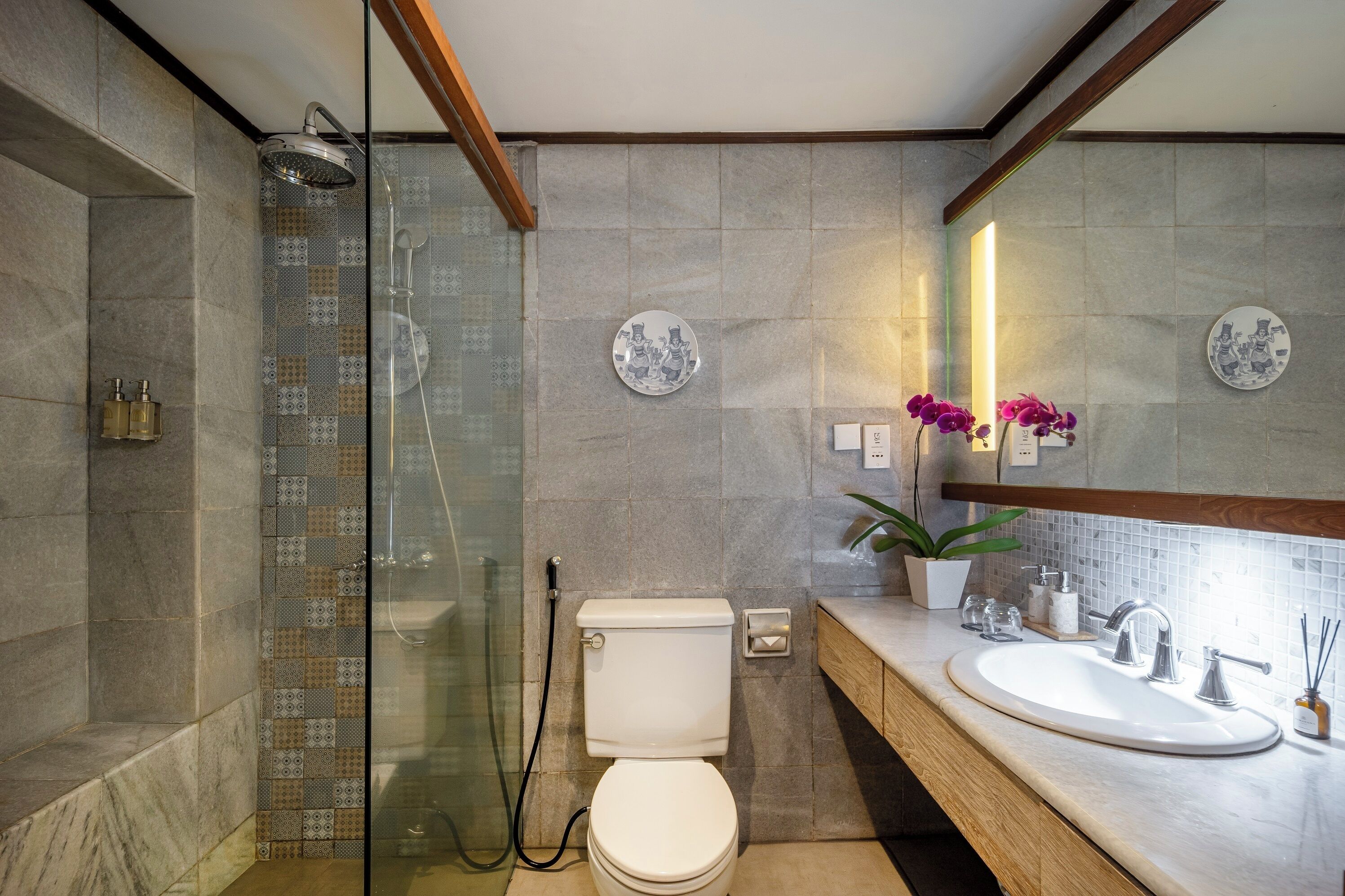 Ein modernes Badezimmer mit einer Glaskabine zur Dusche, einer weißen Toilette und einem Waschbecken mit einer Holzabdeckung.