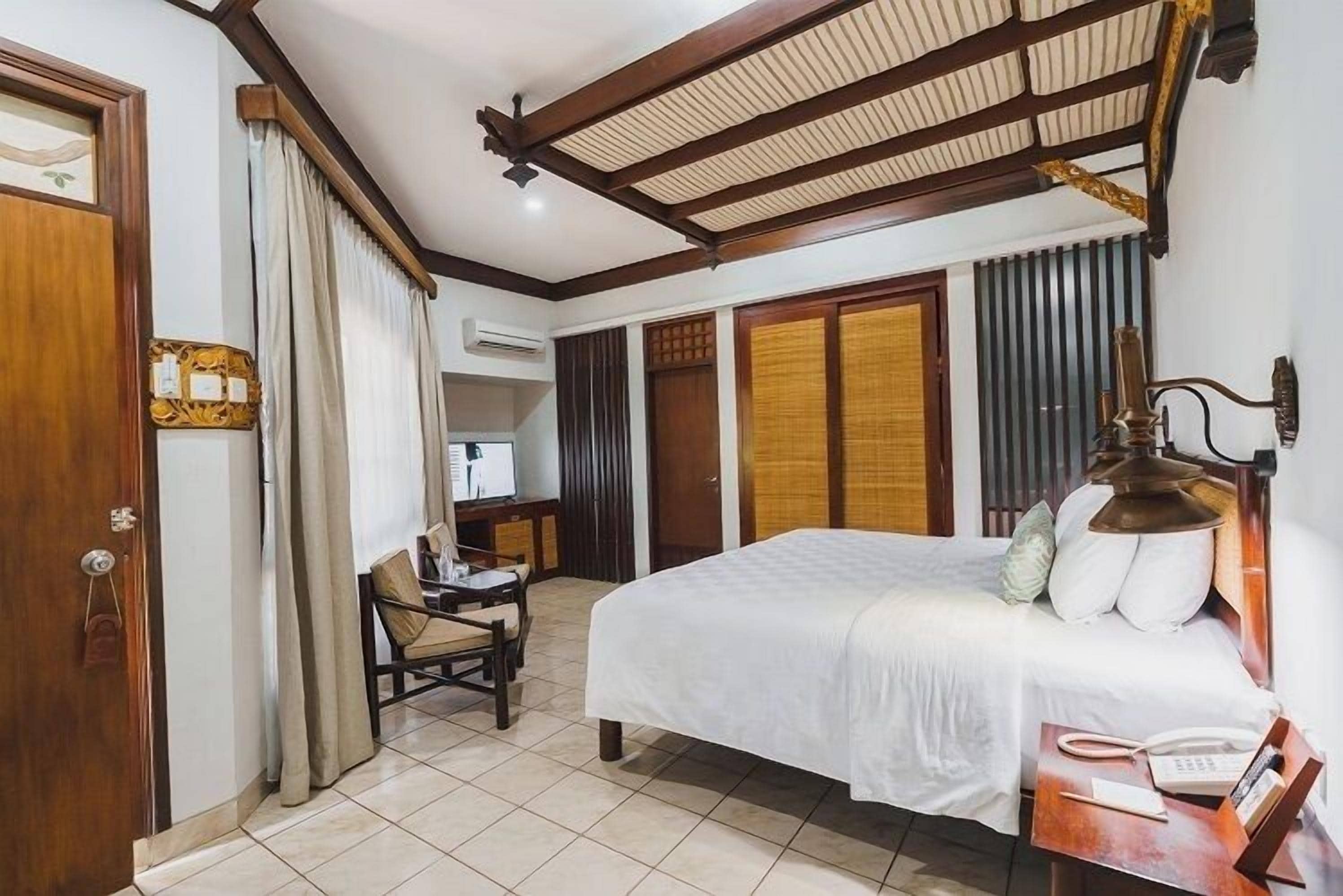 Una habitación de hotel con cama, escritorio, silla, lámpara y armario.