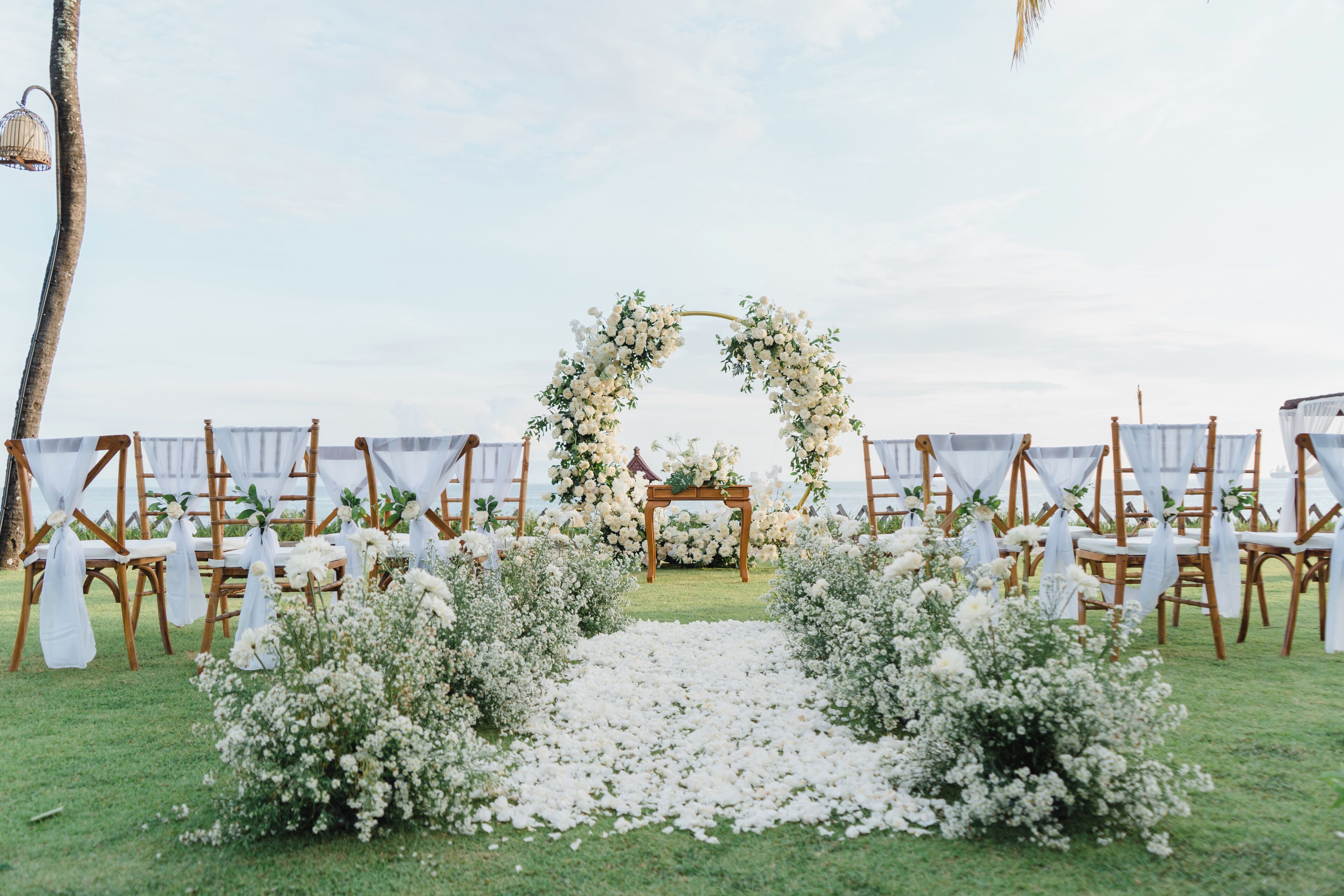 An outdoor wedding ceremony setup with a floral arch, white chairs, and a grassy aisle.
