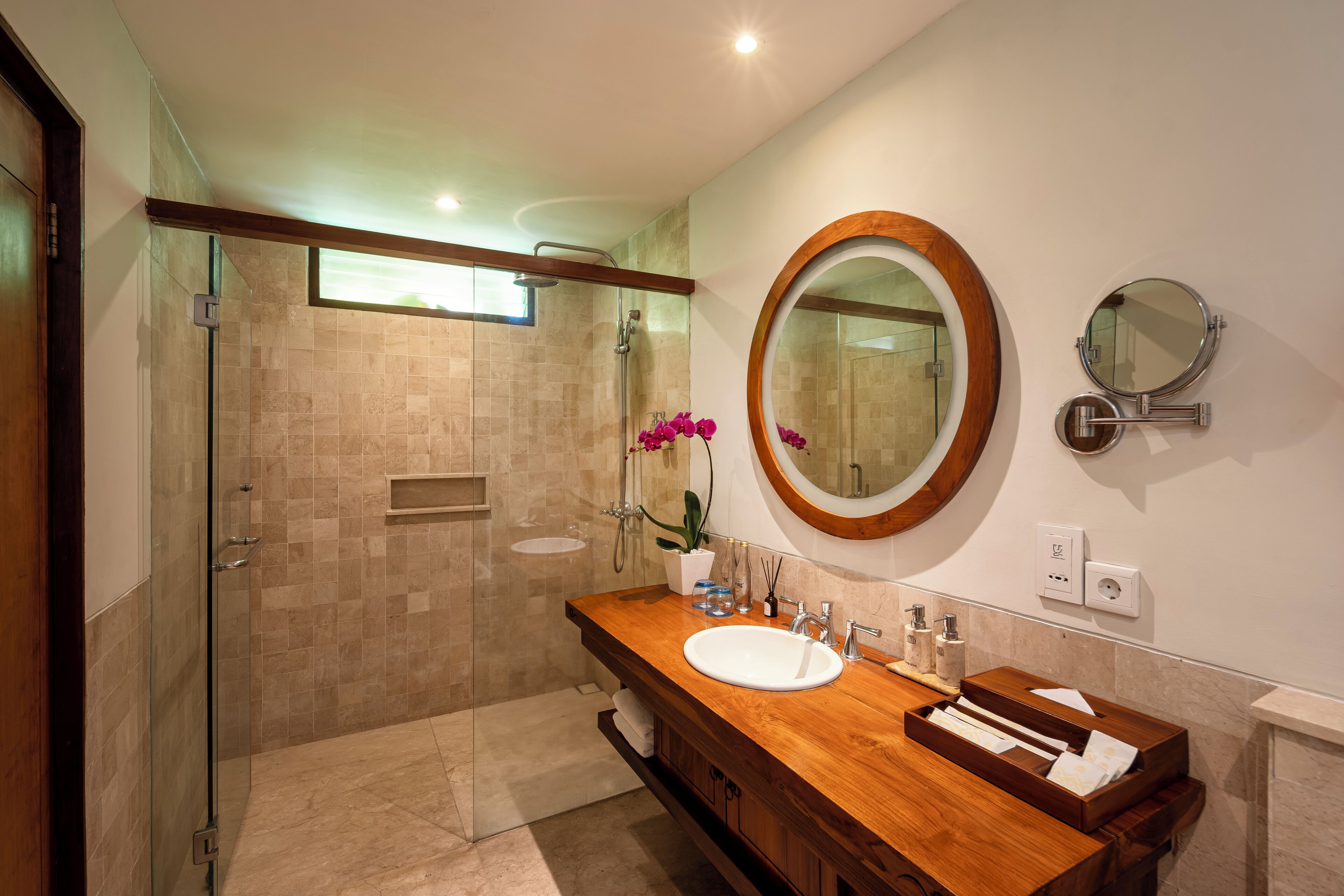 A modern bathroom with a glass-enclosed shower, a wooden vanity with a sink, and a large mirror.