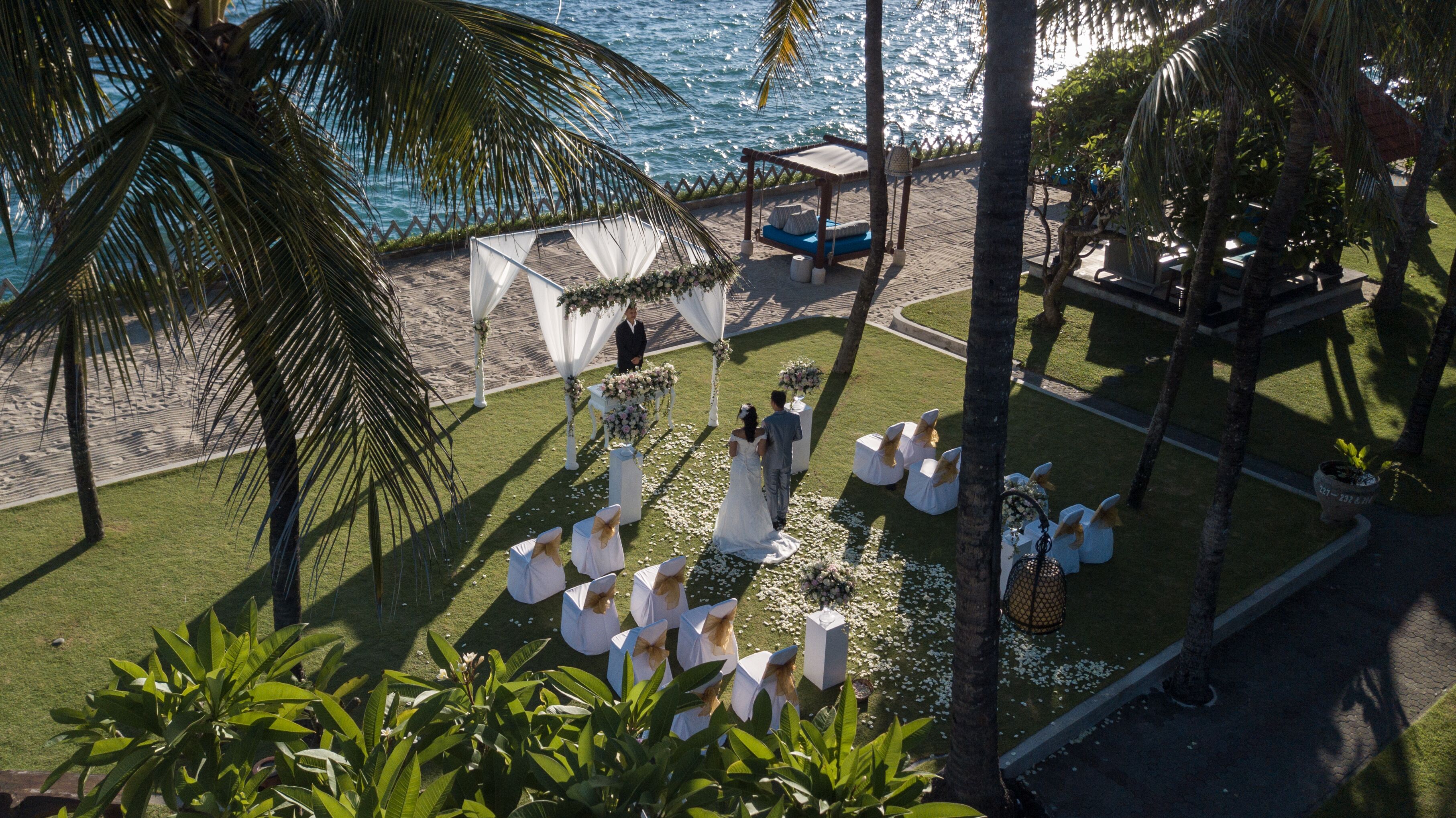 A beach wedding ceremony with a white canopy, guests seated on white chairs, and a view of the ocean.