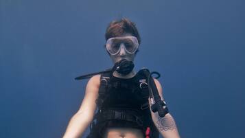 A person in a black wetsuit and scuba gear sitting underwater with a clear blue background.