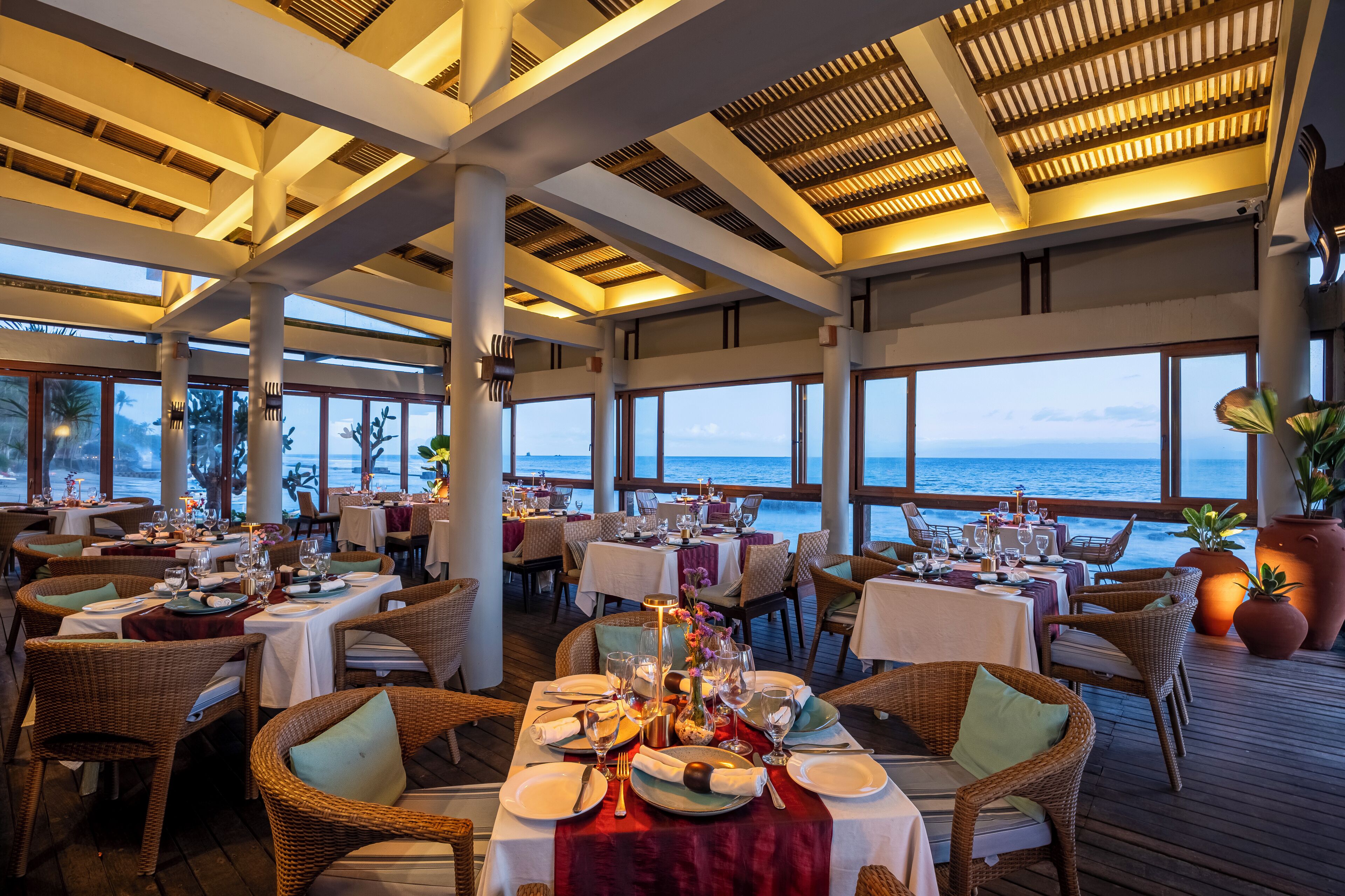 A restaurant with tables set for dining, large windows, and a view of the ocean.