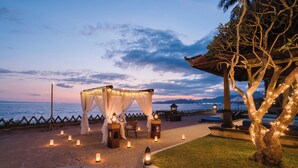 A beachside setup with a canopy, lanterns, and a table under a tree.