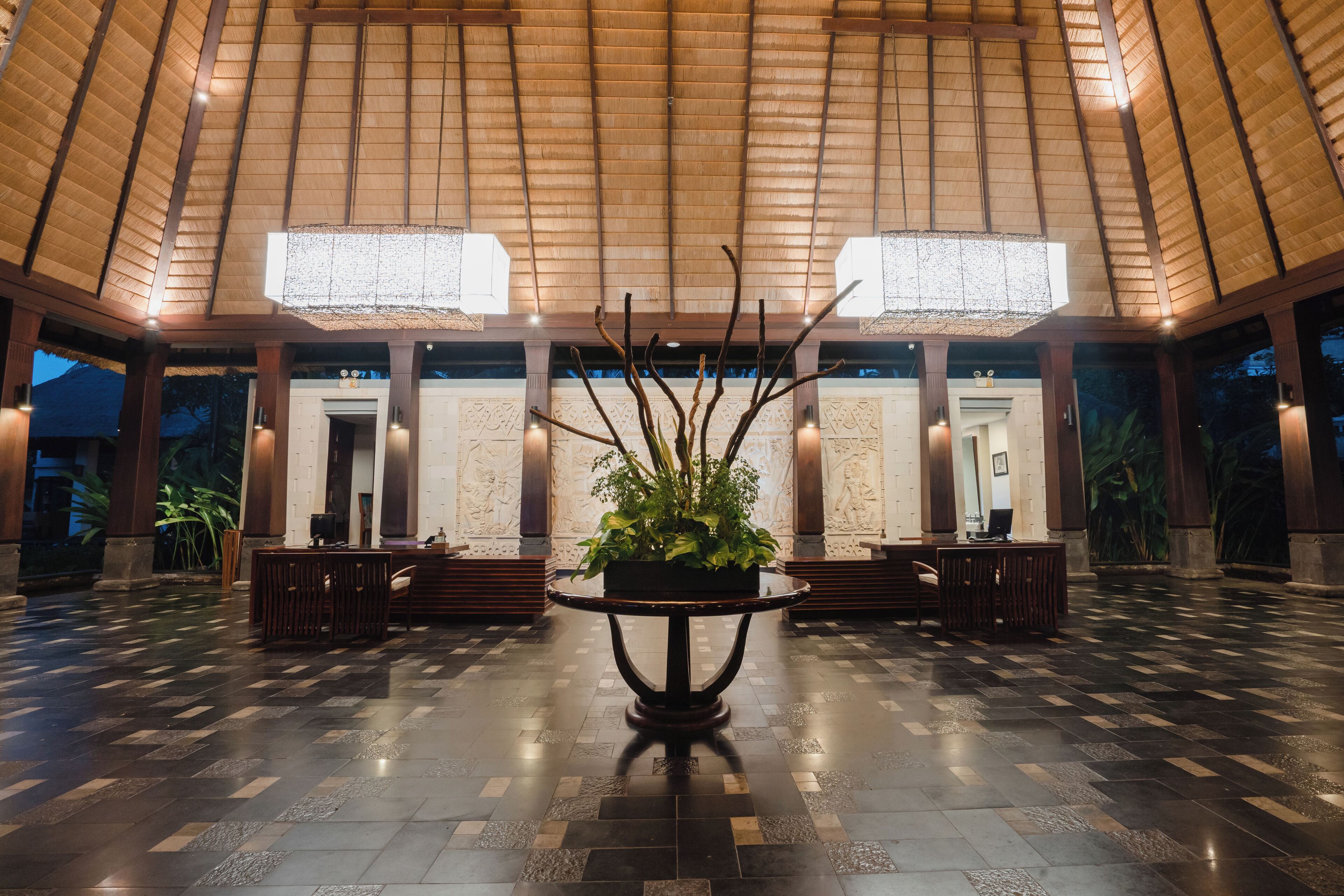 Um hall amplo com teto alto, um arranjo de plantas no centro e um padrão de piso quadriculado.