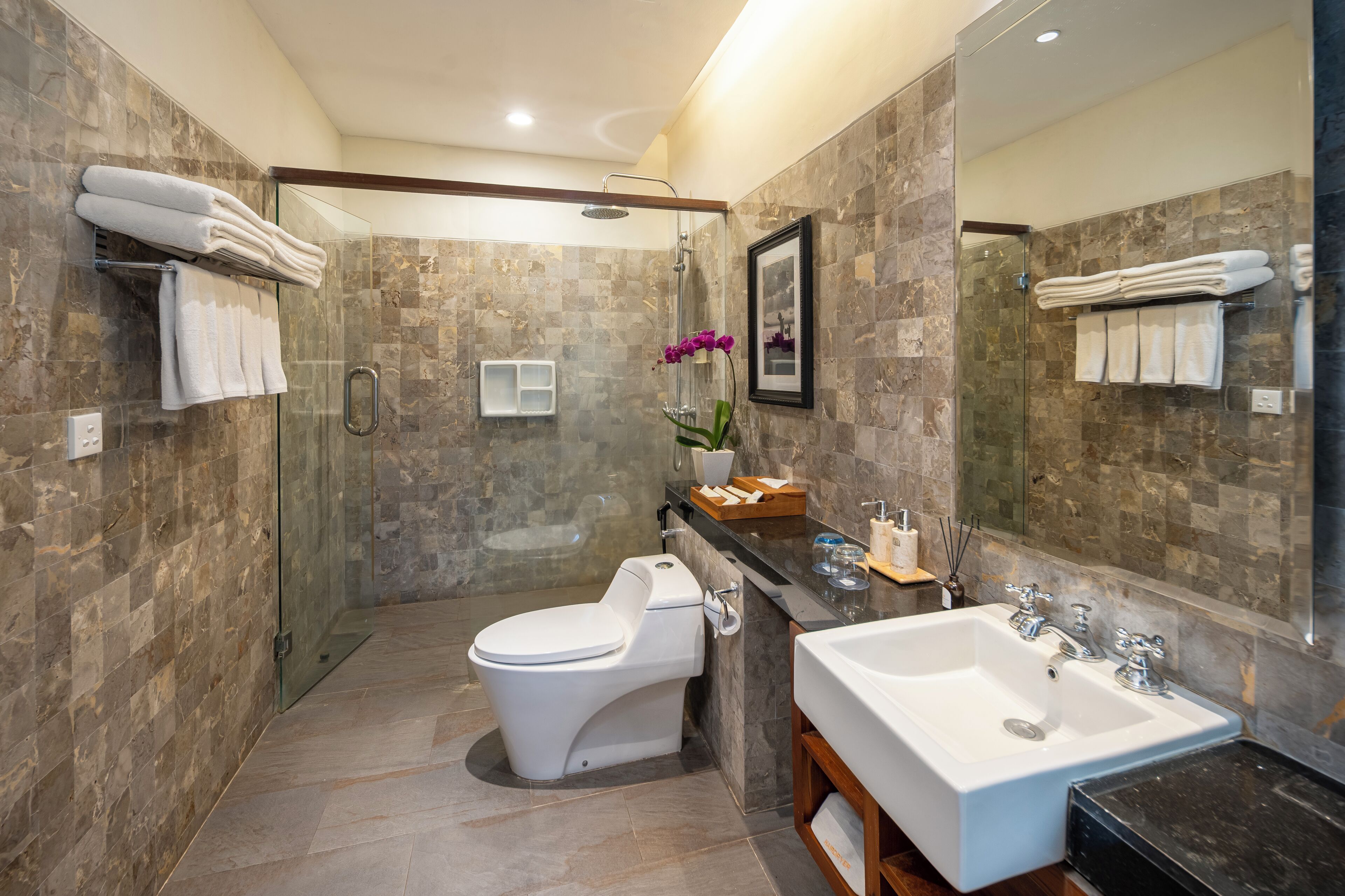 A modern bathroom with a glass-enclosed shower, a white toilet, a large sink, and marble walls.