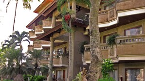 A multi-story hotel with balconies, a garden area with a pond, and outdoor seating.