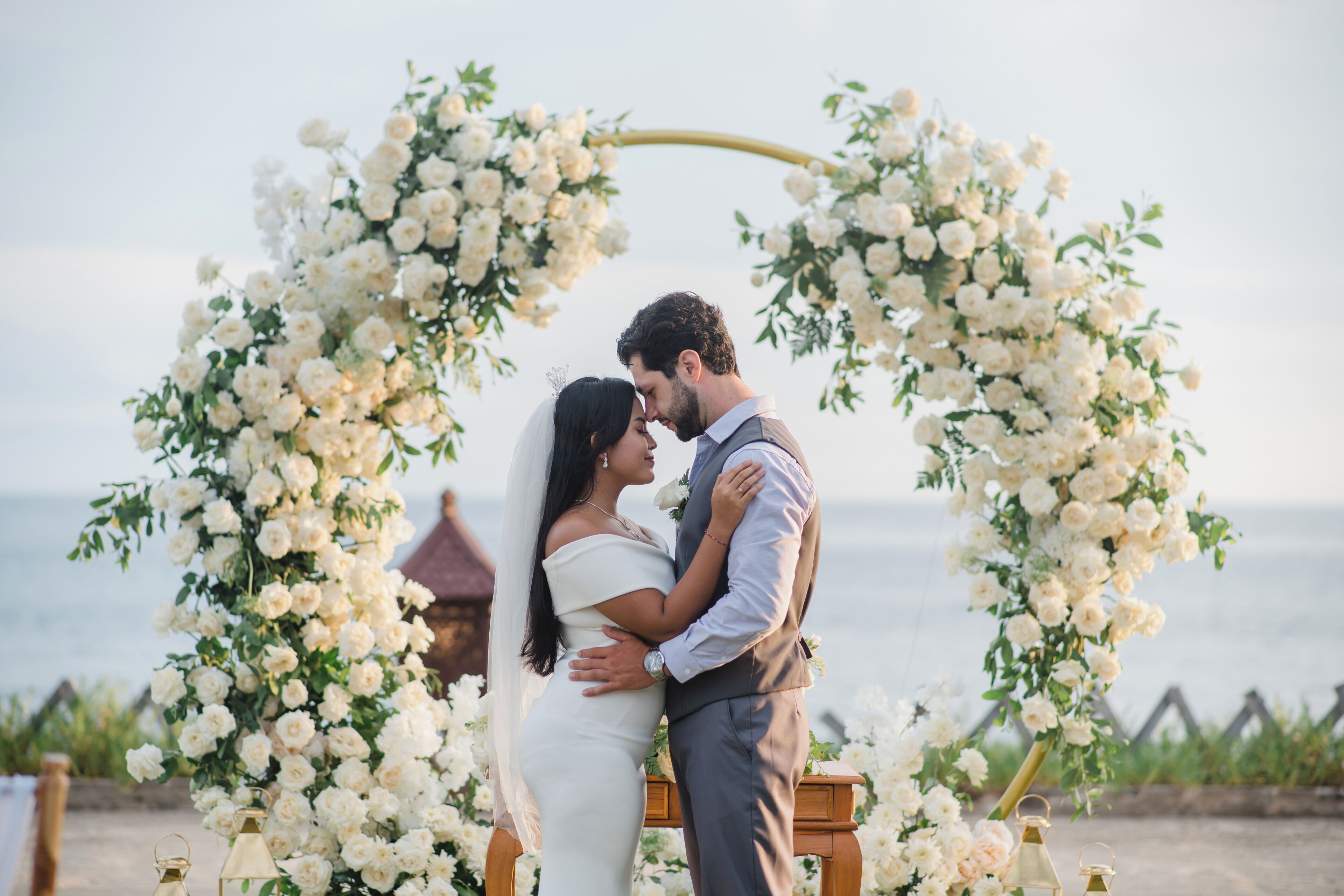 Una pareja abrazándose bajo un arco floral, con vista al mar.
