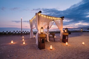 Escena de playa con una toldo, mesas, velas y un farol.