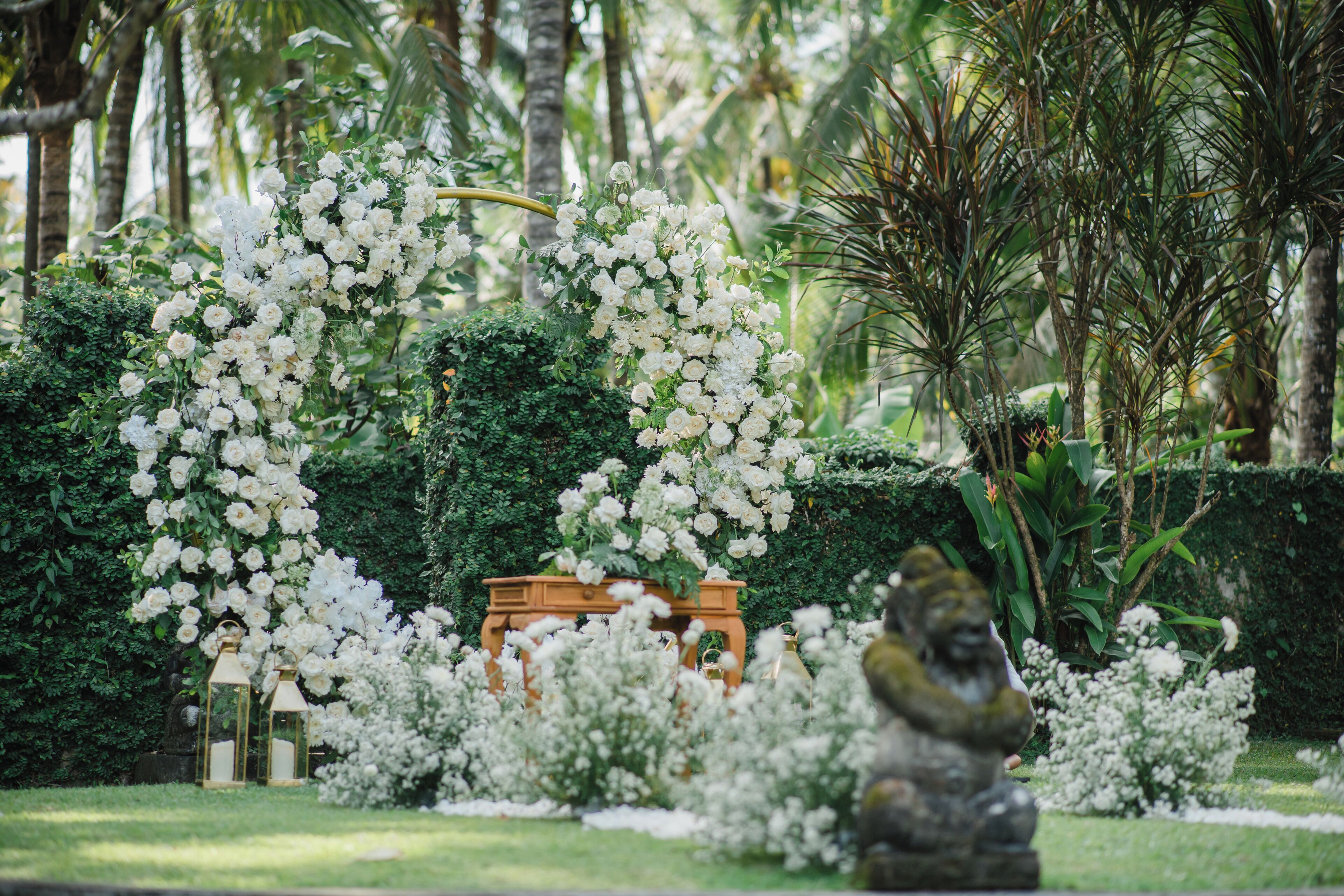 A garden with white flowers, a statue, and a wooden bench.
