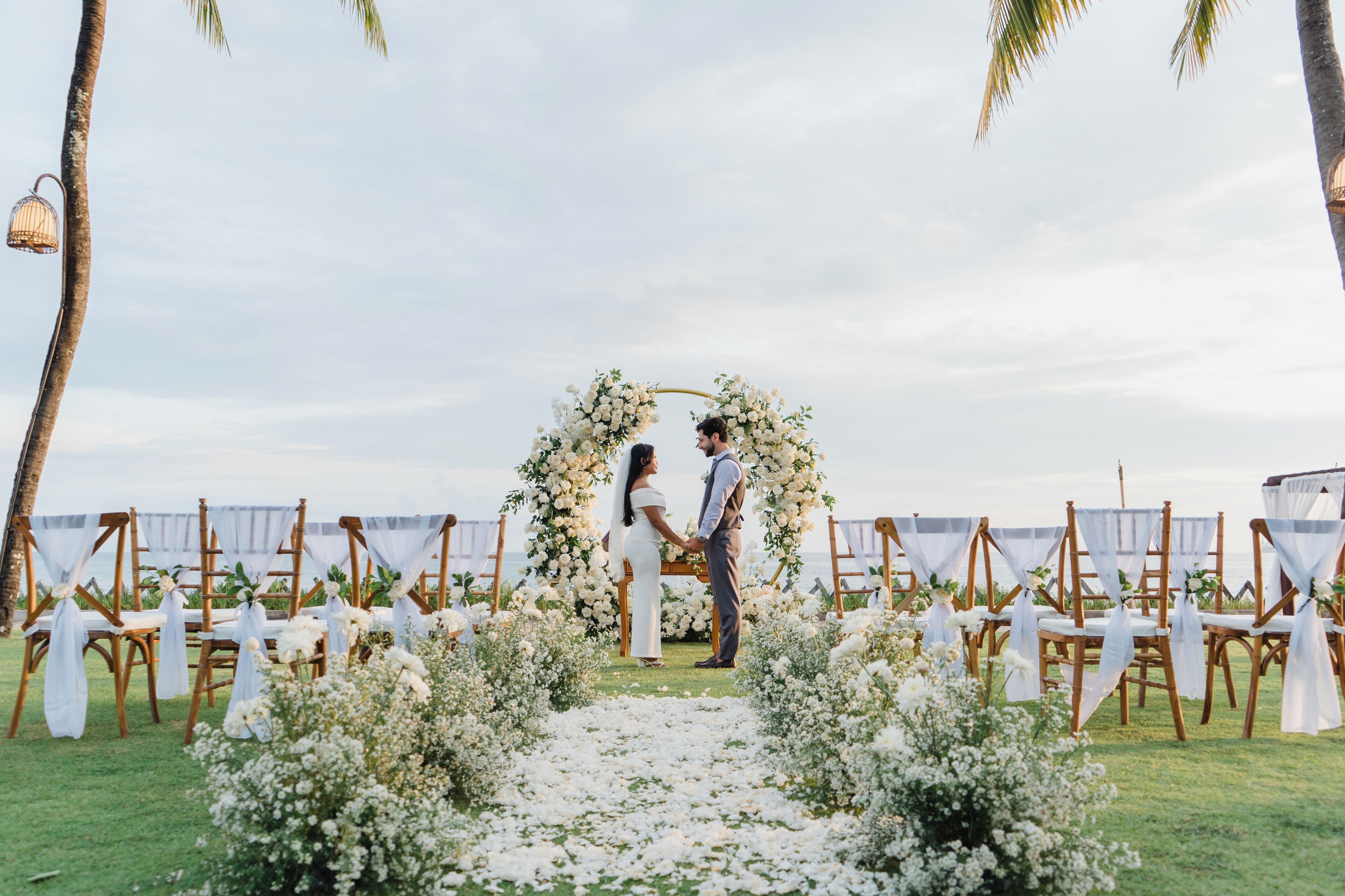 A wedding ceremony with a floral arch and chairs arranged on a grassy area.