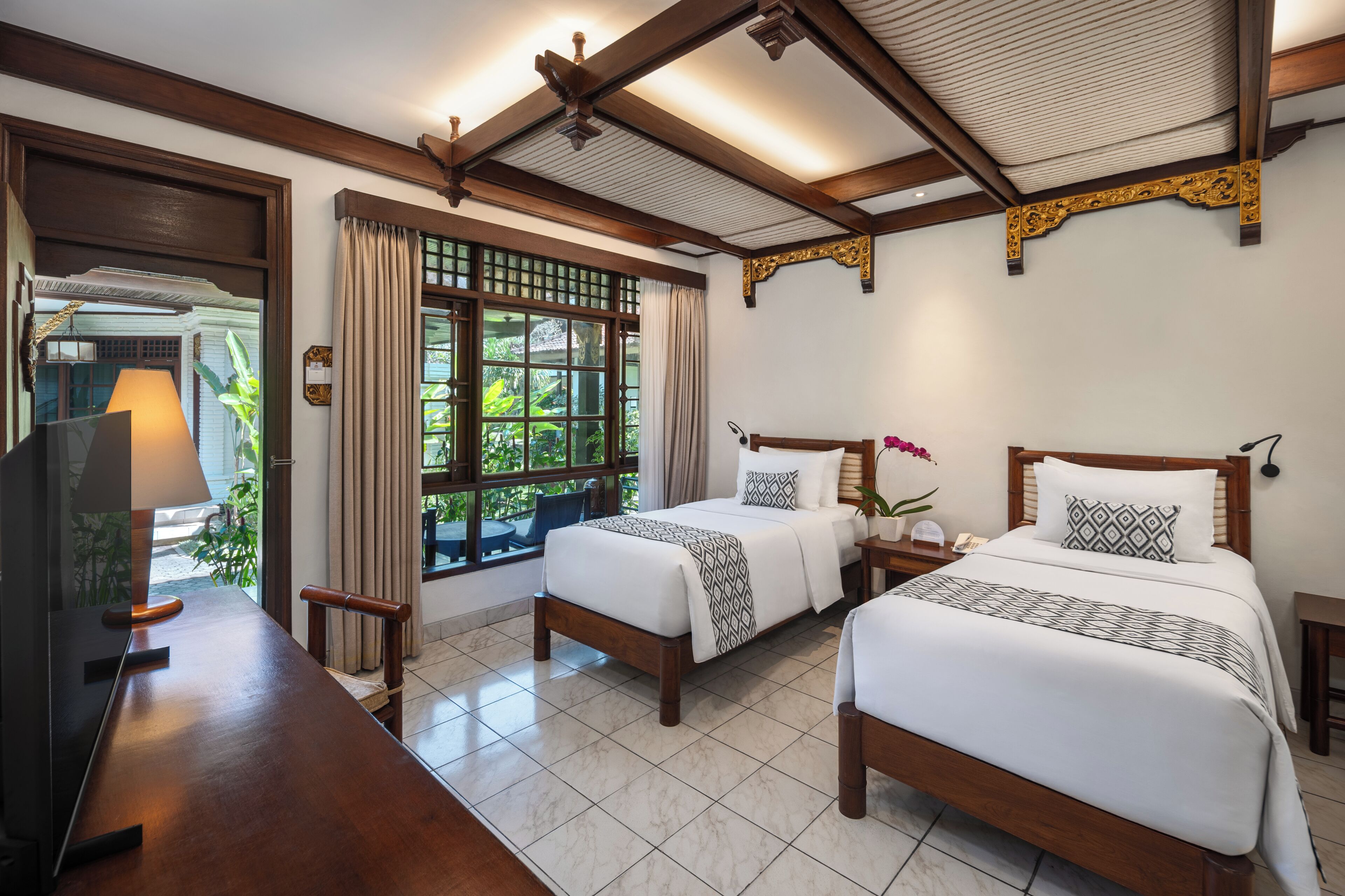 Habitación de hotel con dos camas, un escritorio de madera, televisor y ventana con cortinas.