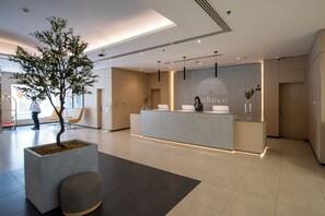 A modern reception area with a reception desk, a potted tree, and a seating area. - Radiance Premium Suites (Dubai)