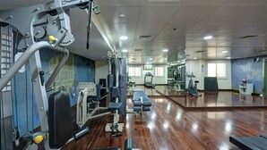 Een fitnessruimte met trainingsapparatuur, een spiegelwand en een houten vloer.