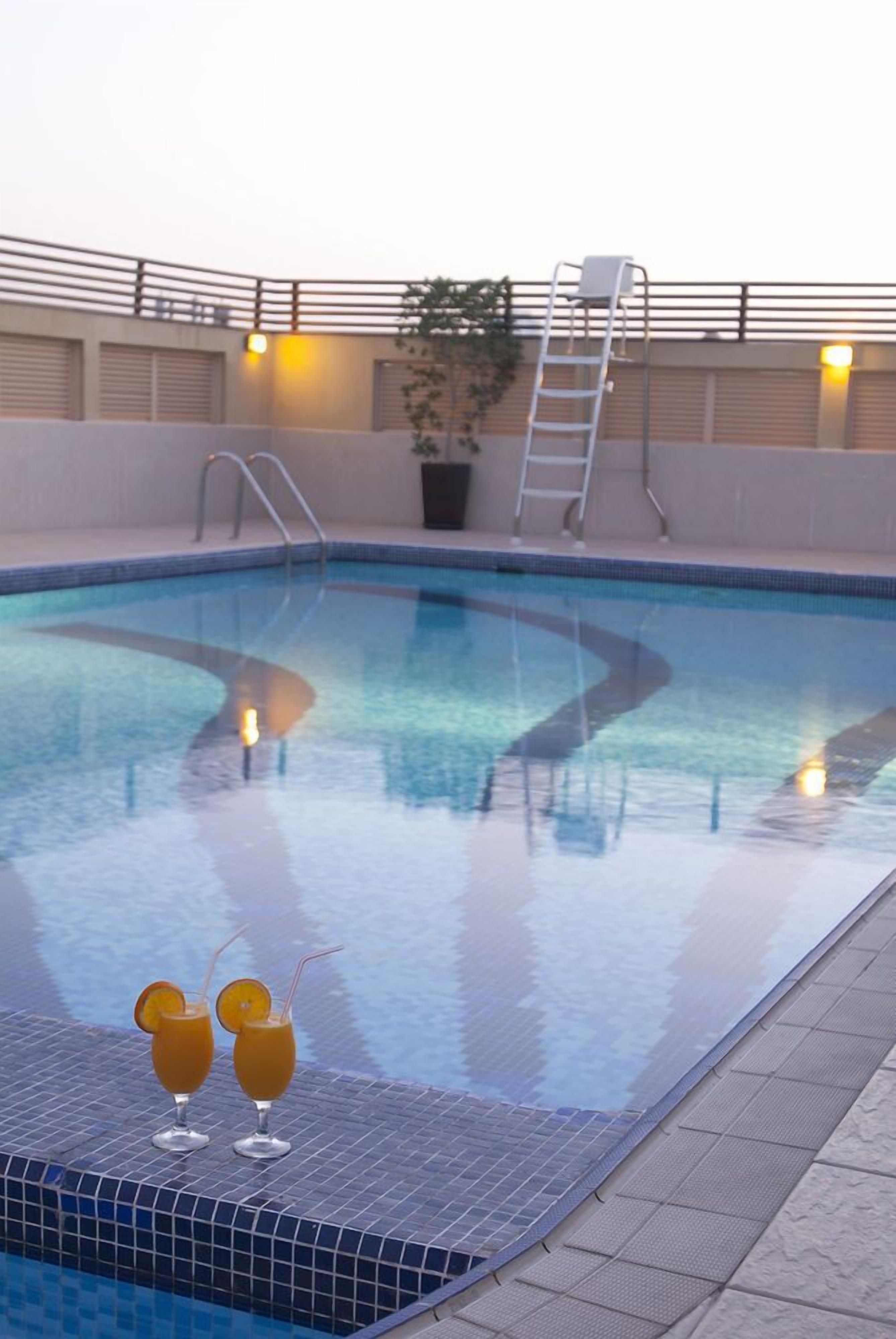 Una piscina con dos bebidas en el borde, una escalera y una barandilla.