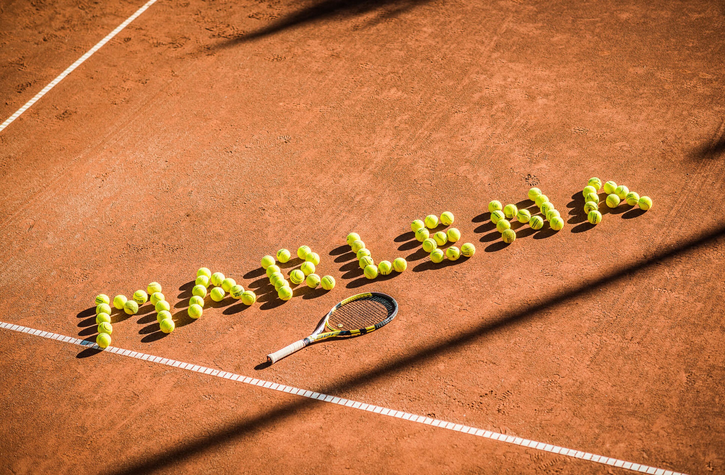Una cancha de tenis con pelotas amarillas dispuestas en un diseño y una raqueta sobre el suelo.