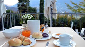 A table set with breakfast items including croissants, a bowl, a cup, and a jug of orange juice, with a mountain view in the background.