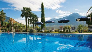 A swimming pool with lounge chairs and umbrellas, surrounded by palm trees and mountains in the background. - Hotel Marlena (Marlengo)