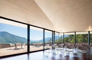 Amplia habitación con grandes ventanales que ofrecen vistas a la montaña, una terraza de madera y un mobiliario moderno.