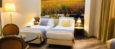 A hotel room with two beds, a desk, a chair, and a large painting of a sunset over a field of poppies.