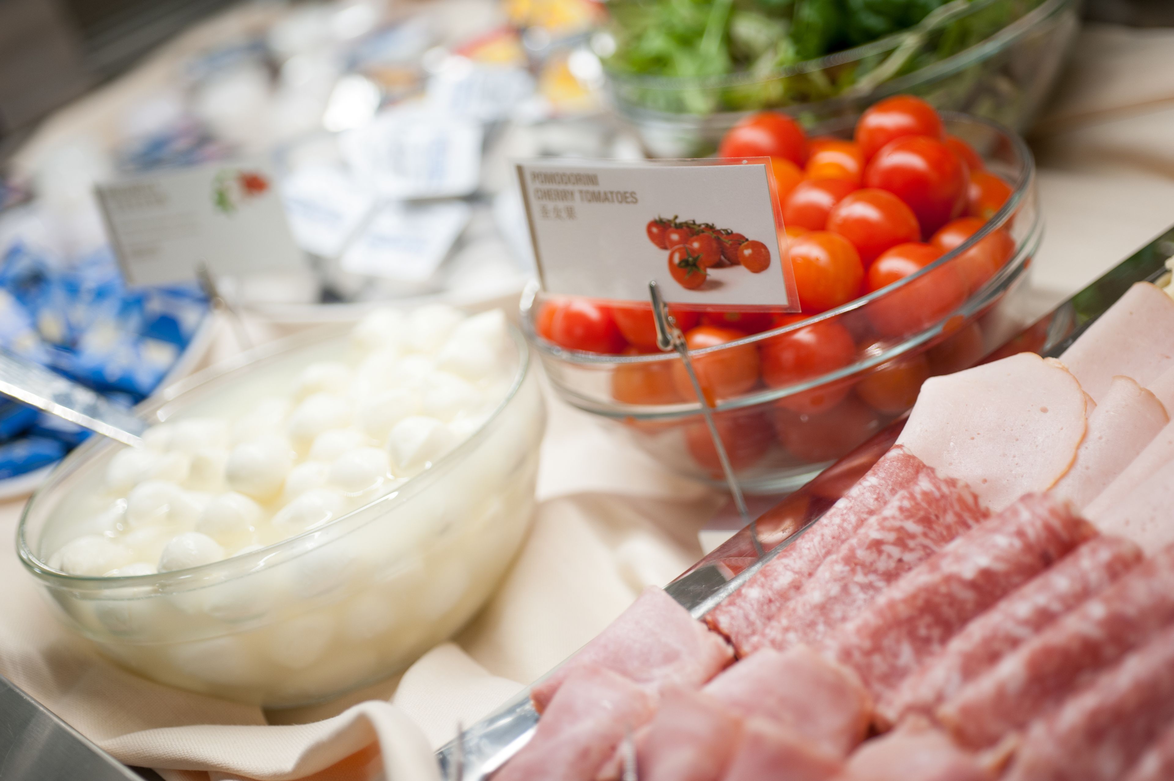 A buffet with various food items including cherry tomatoes, a bowl of white cheese balls, and sliced meats.