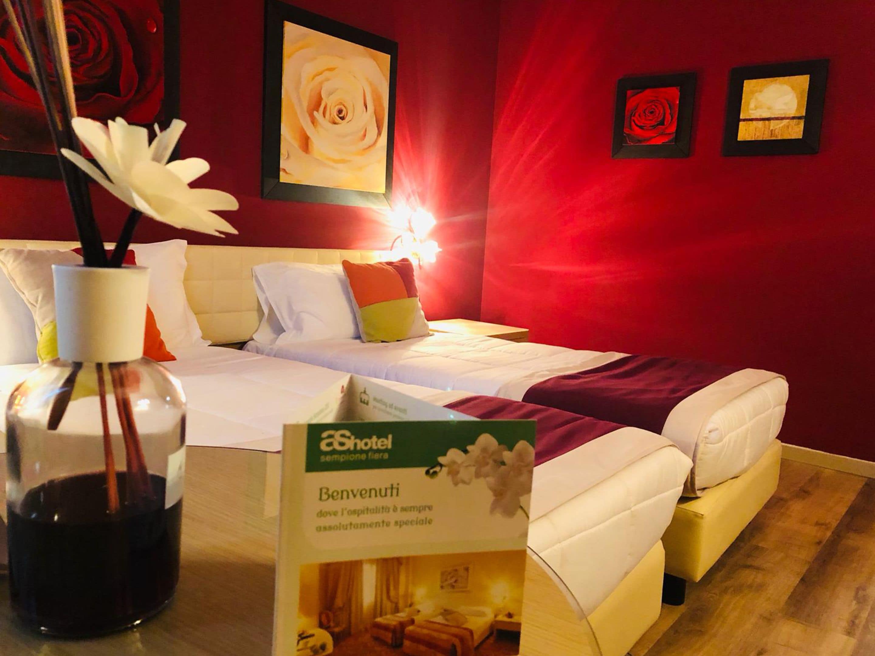 A hotel room with two beds, a vase with white flowers, and a sign welcoming guests.
