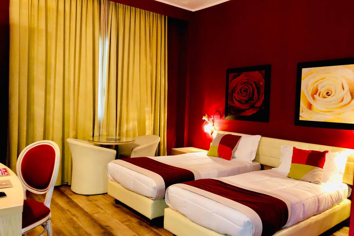 A hotel room with two beds, a desk, a chair, and a large window with curtains.