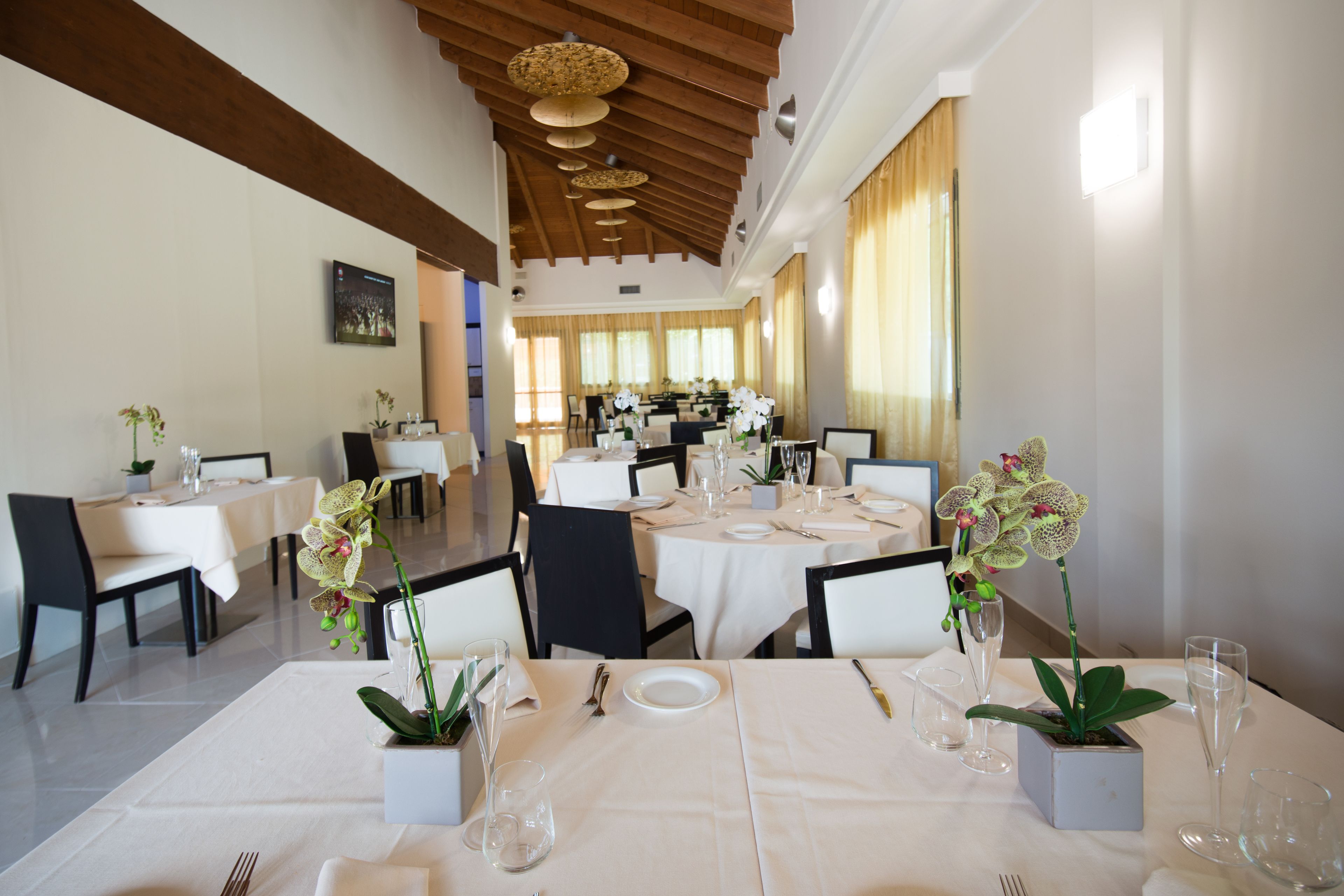 A dining area with tables set for service, featuring white tablecloths, chairs, and orchid centerpieces.