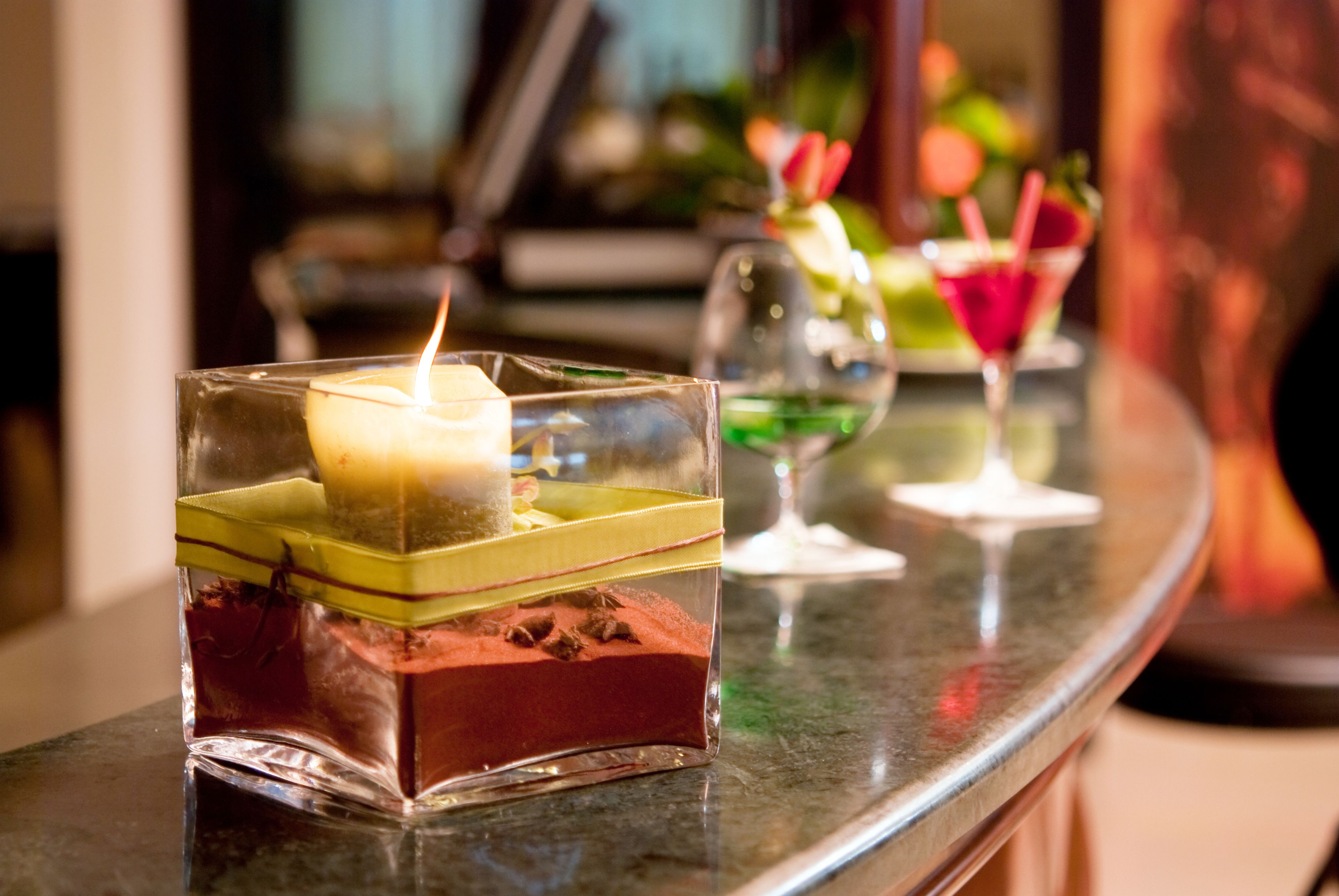 A bar area with a candle in a glass container, a martini glass, and a cocktail with a straw.