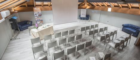 Un salón de conferencias con un escenario, filas de sillas, un sofá azul y una araña.