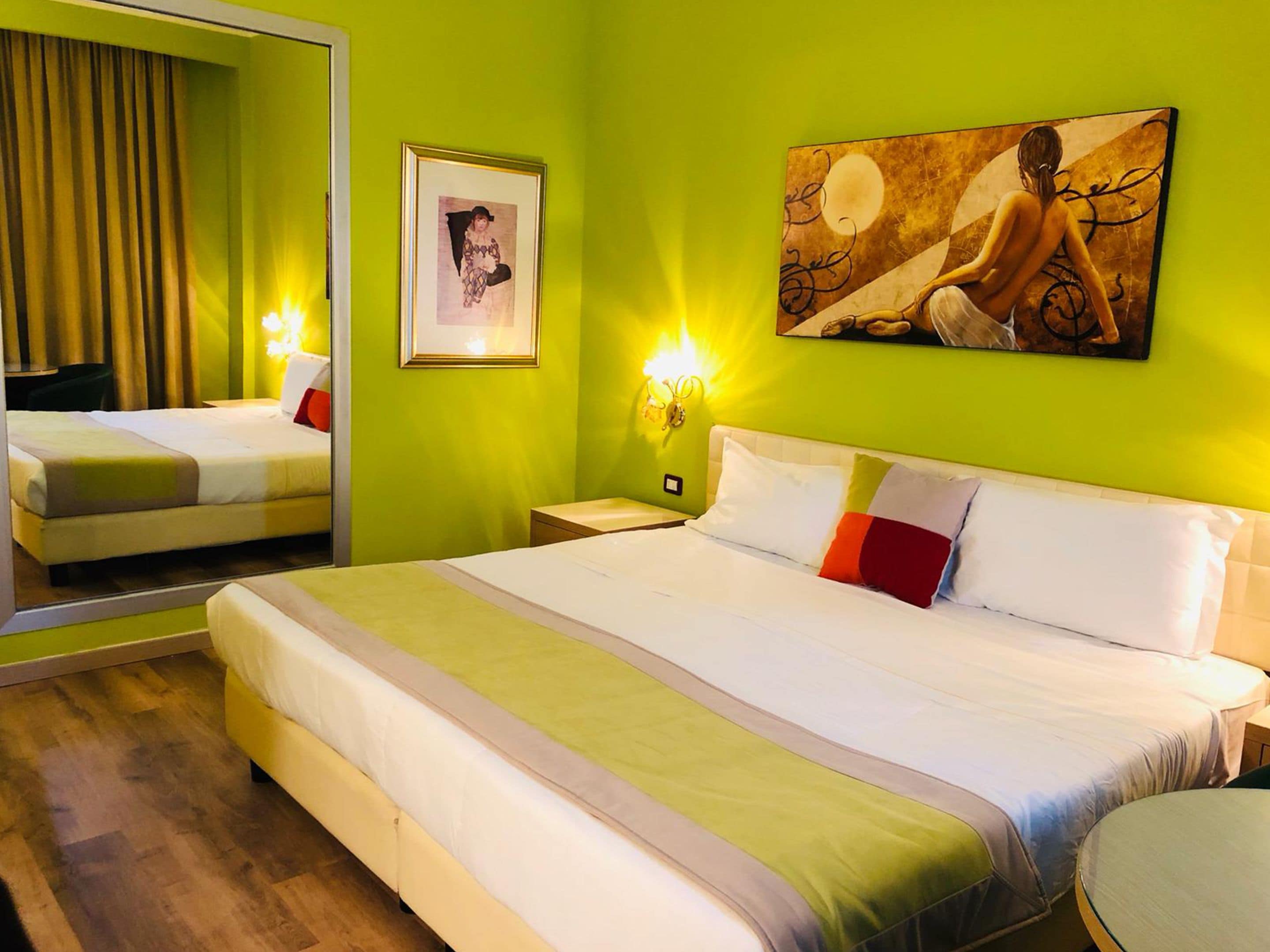 Habitación de hotel con una cama grande, un espejo, un cuadro enmarcado y una lámpara de pared.