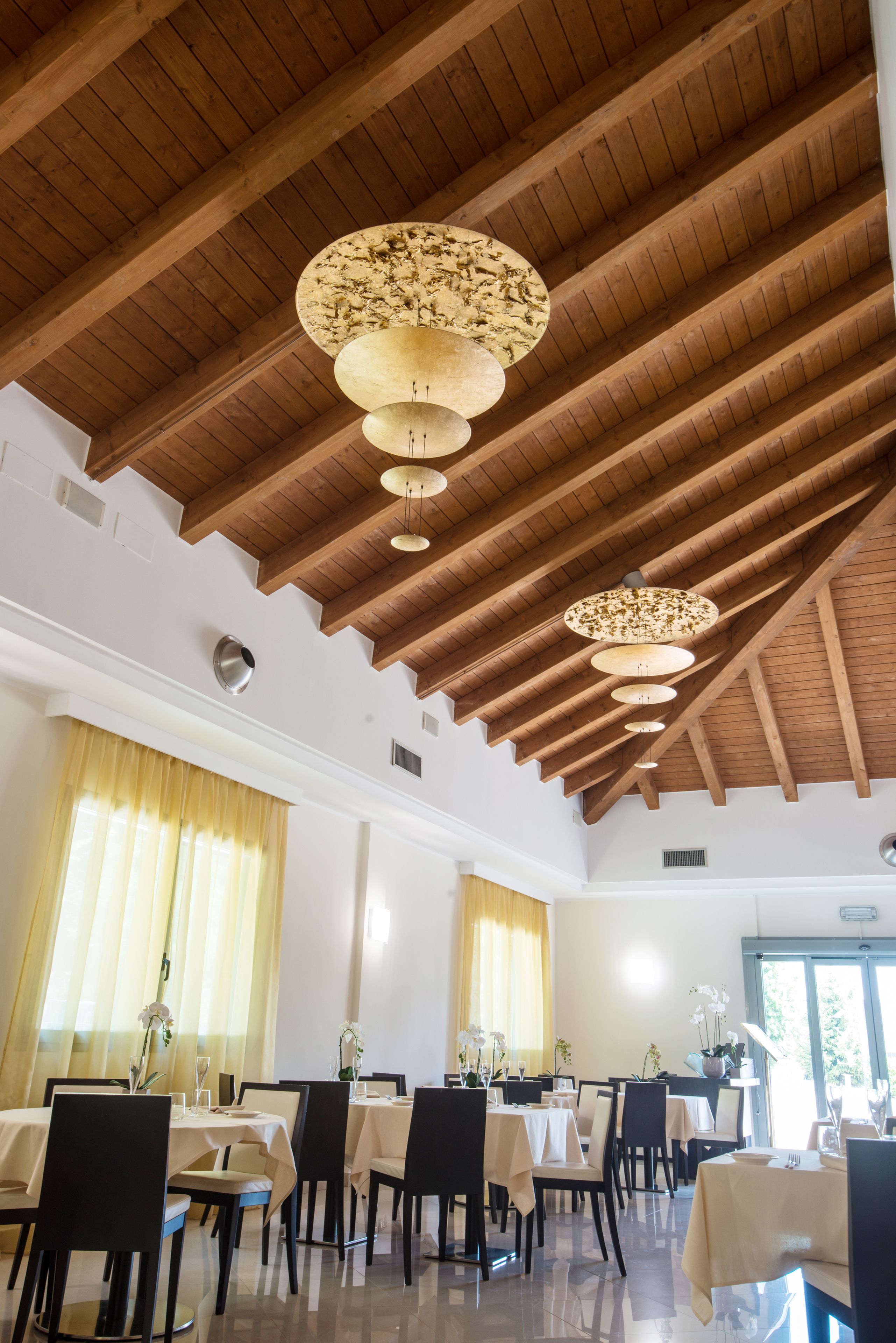 Un comedor con vigas de madera y candelabros. Las mesas están dispuestas con manteles blancos y sillas negras.