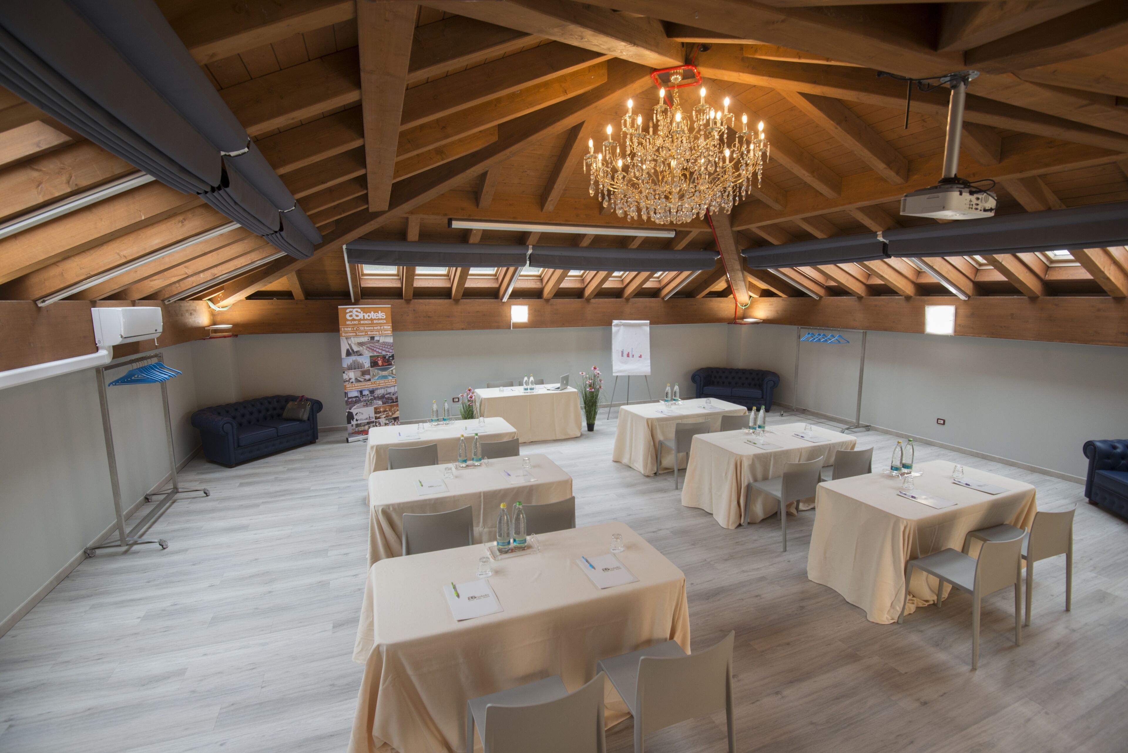 Un salón de conferencias con mesas, sillas, una araña y un proyector.