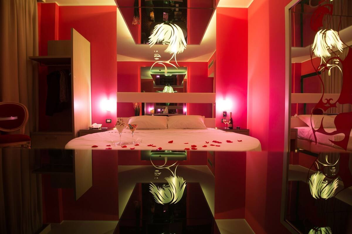 A modern hotel room with a large bed, a mirror, and a red color scheme.