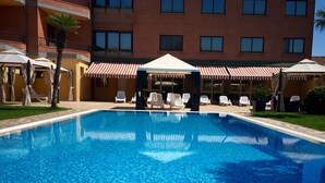 A swimming pool with lounge chairs and umbrellas, surrounded by a building with multiple windows and balconies.