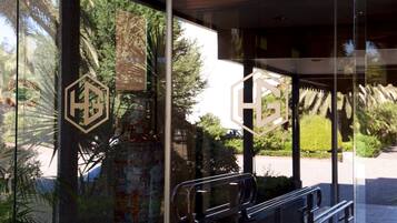 A glass door with a logo, a metal handrail, and a view of greenery outside.