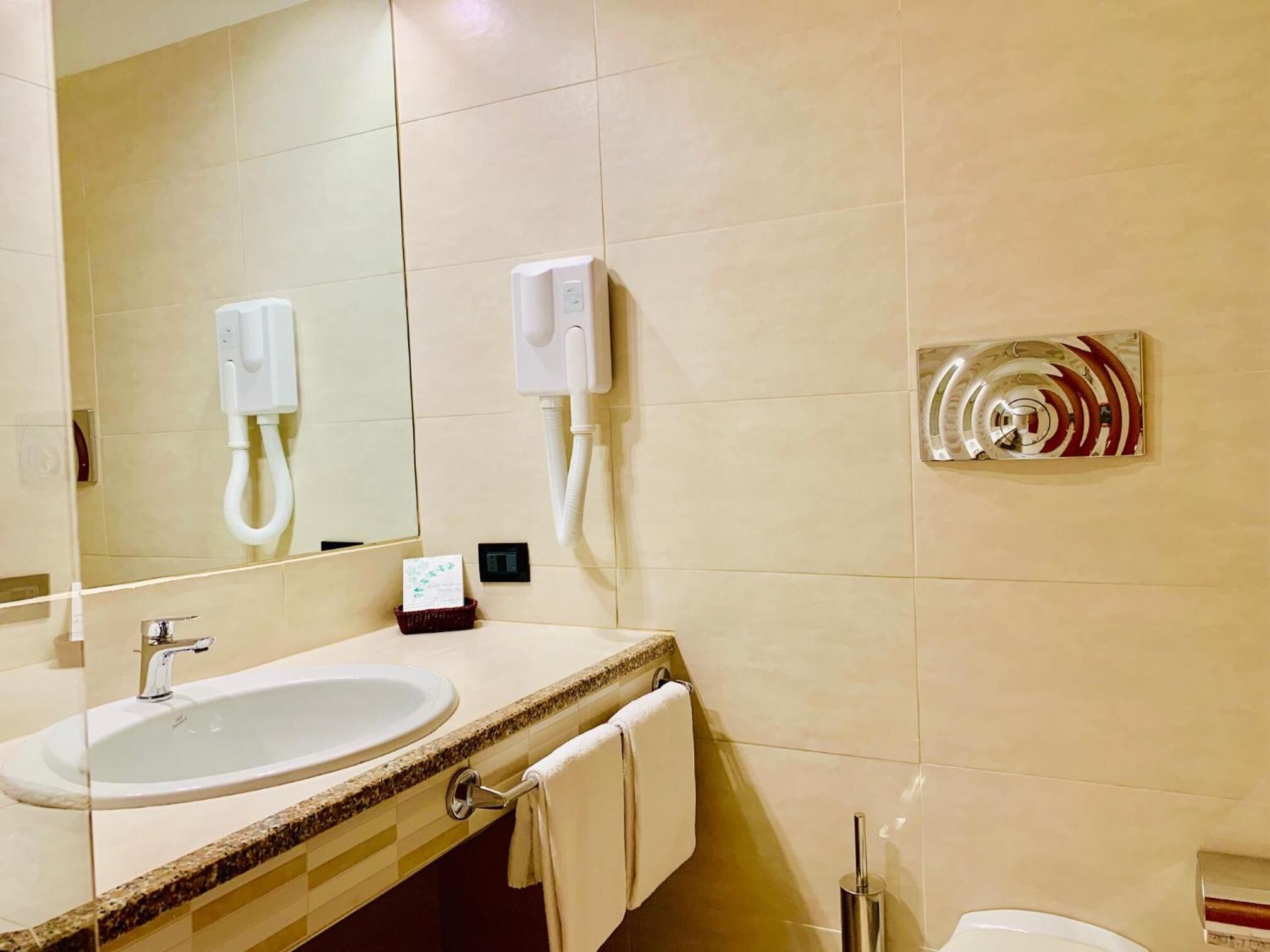 Ein Badezimmer mit Waschbecken, Spiegel, Handtuchhalter und einem Händetrockner.