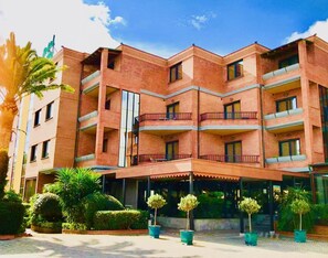 Un hotel de varios pisos con fachada de ladrillo, balcones y un área de entrada cubierta.