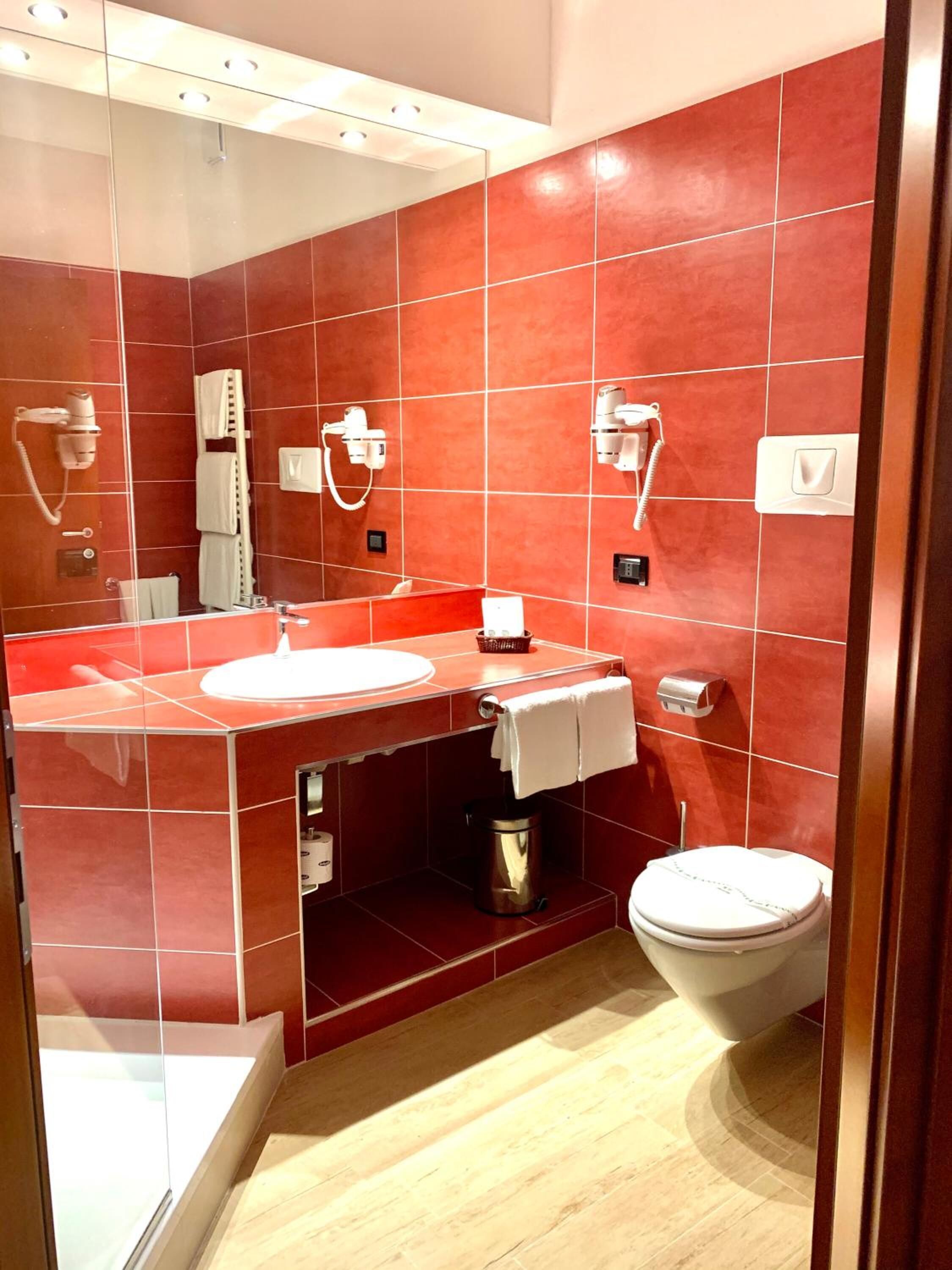 Een moderne badkamer met een grote spiegel, een wastafel, een toilet en twee haardrogerhouders aan de muur.