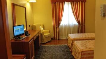 A hotel room with a desk, chair, two beds, a large window with curtains, and a television.
