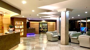 A spacious lobby with a reception desk, seating area, and a visible kitchen in the background.