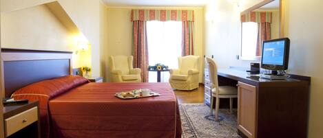 A hotel room with a large bed, two chairs, a desk with a computer, and a small table with a vase of flowers.