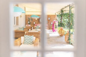 Un espacio interior acogedor con muebles de mimbre, una bicicleta rosa y una planta colgante.