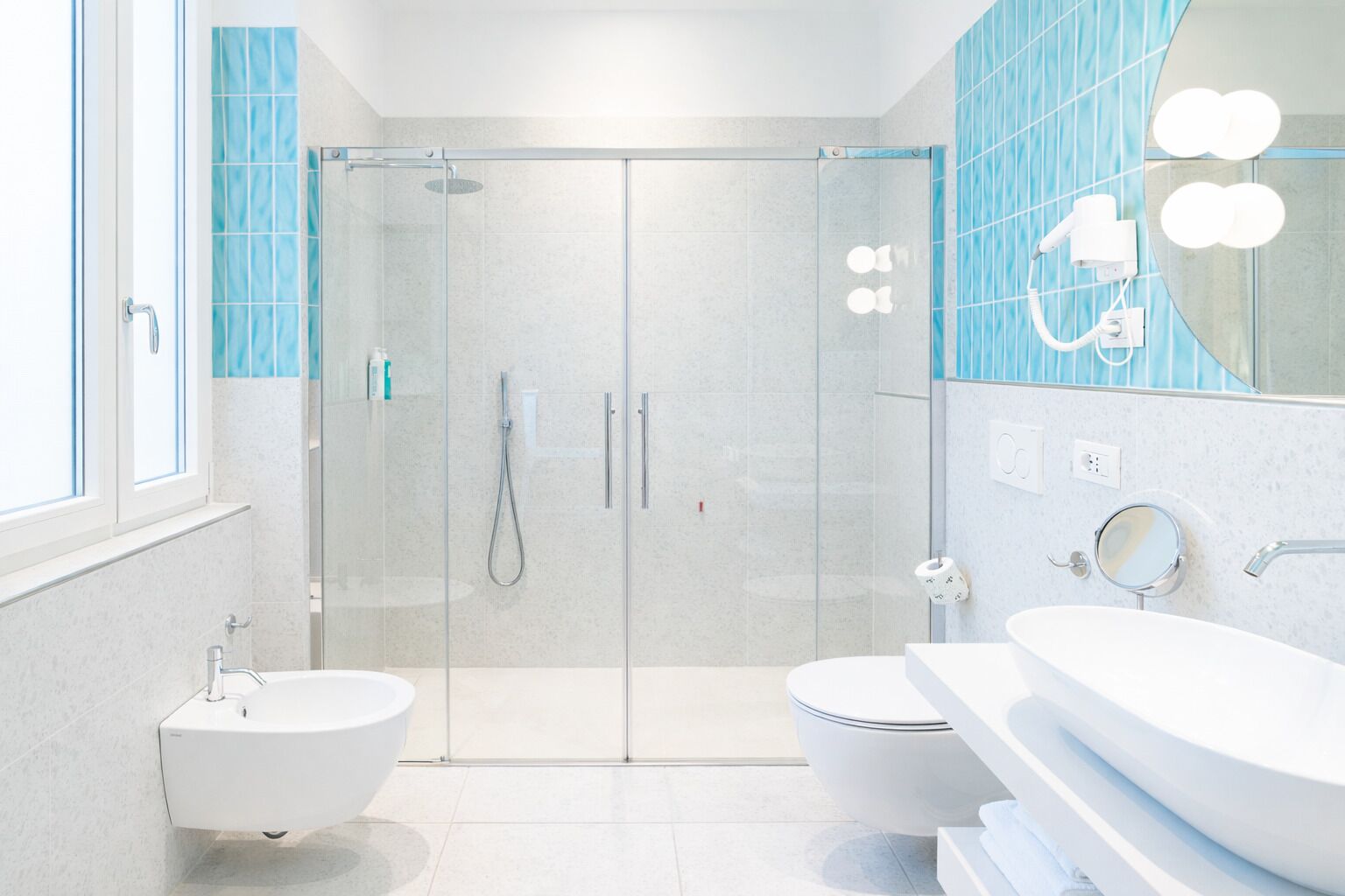 Un bagno moderno con doccia vetrata, due lavabi, uno specchio grande e una finestra.