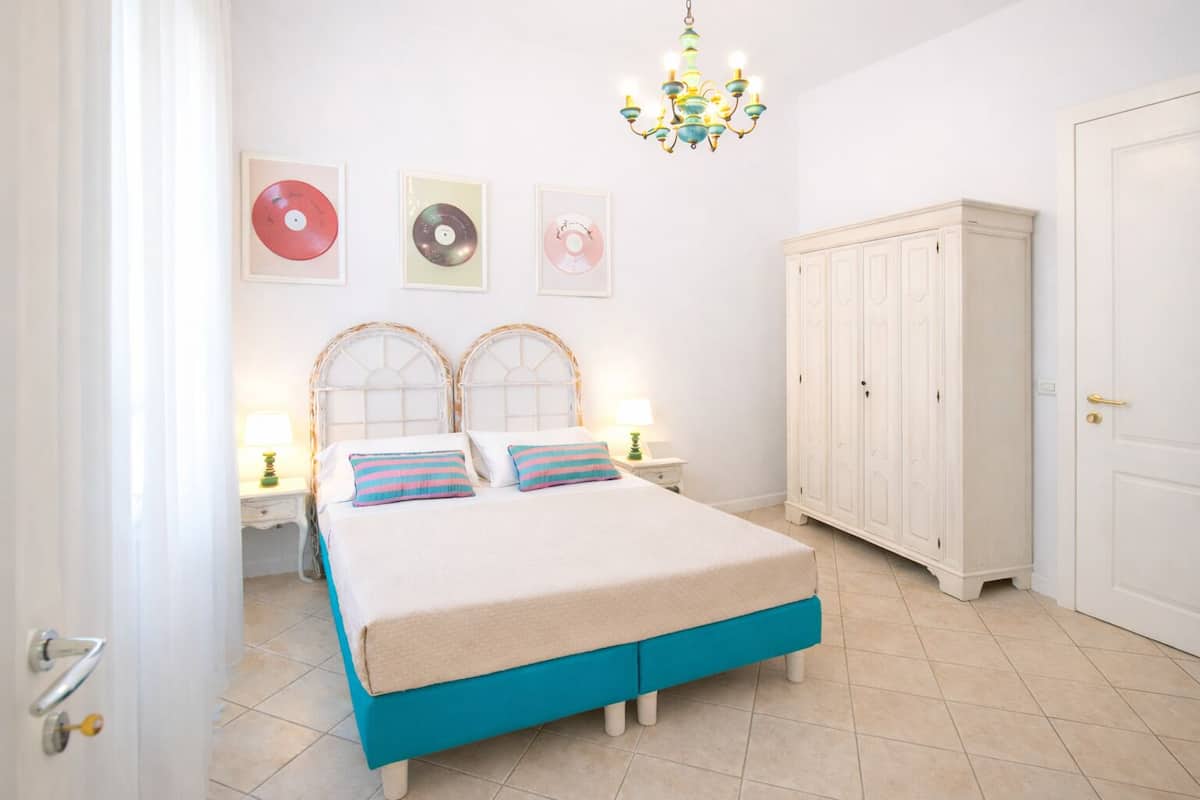 Une chambre à coucher avec un lit, des tables de chevet, une armoire et un lustre.